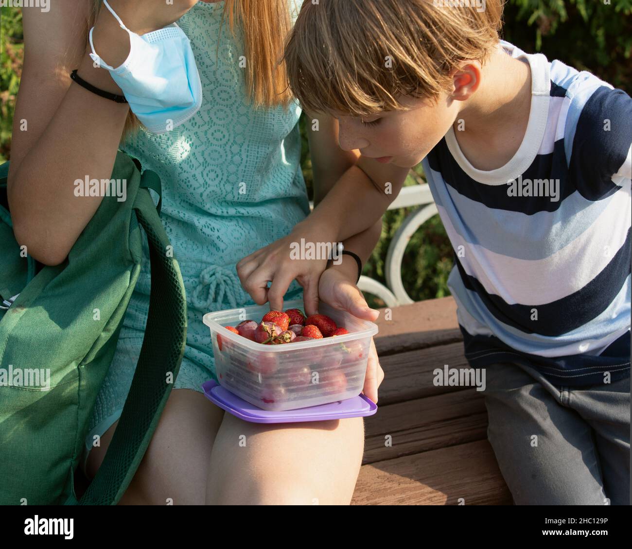 Giovane caucasico ragazzo e ragazza nel parco pubblico mangia frutti estivi e bacche durante la pandemia del virus del coronavirus Foto Stock