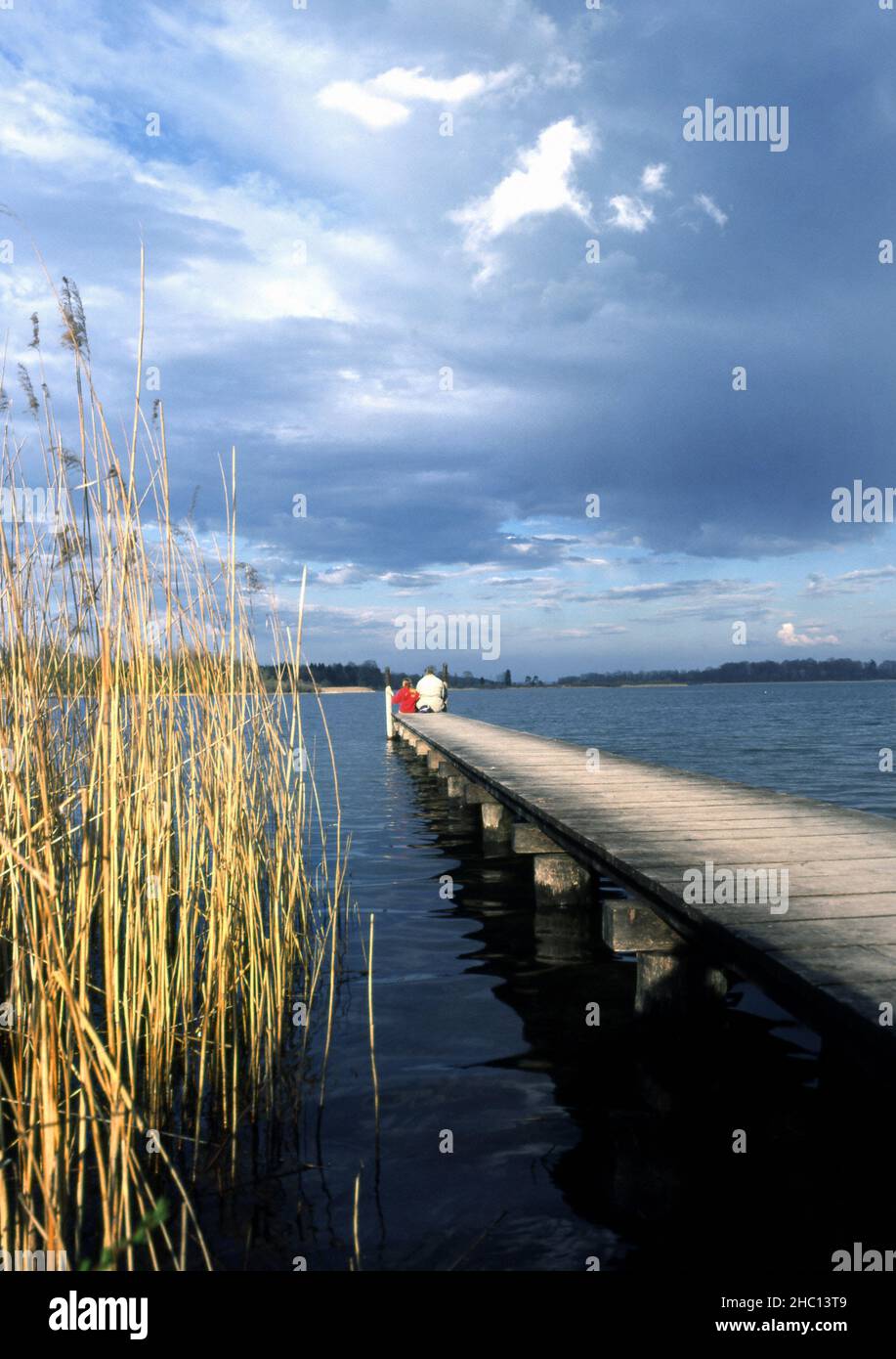 Uomo e ragazza seduti alla fine di un piccolo molo di legno, molo, Chiemsee, Baviera, Germania Foto Stock