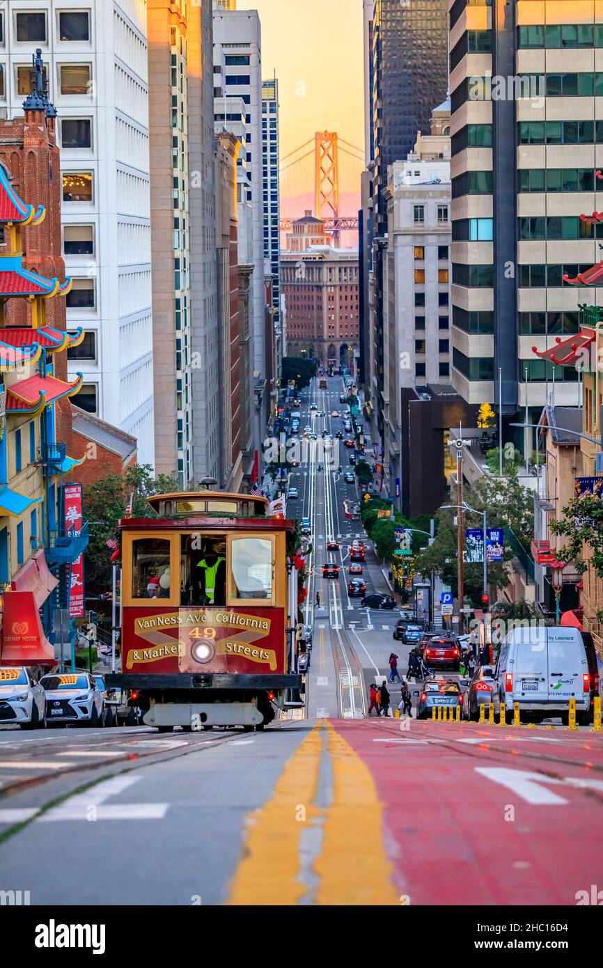 San Francisco, USA - Dicembre 18 2021: Vista famosa di una funivia su California Street vicino a China Town con il Bay Bridge sullo sfondo al tramonto Foto Stock
