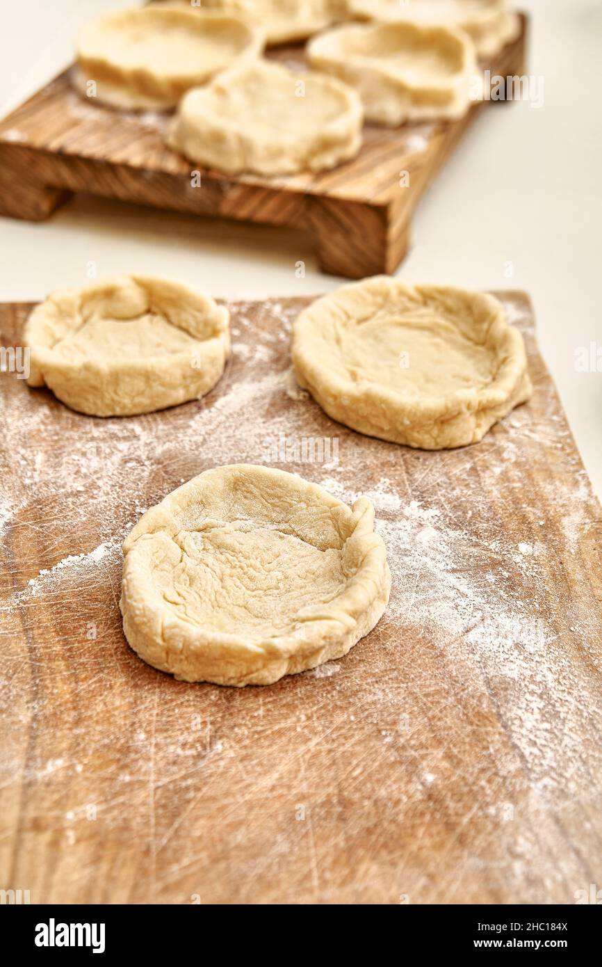 Torte forme di pasta cruda preparate per aggiungere diversi riempitivi su tavole rustiche di legno su tavola bianca in cucina vista ravvicinata Foto Stock