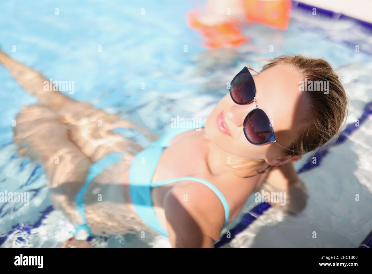 Felice giovane femmina seduta in piscina con occhiali alla moda Foto Stock