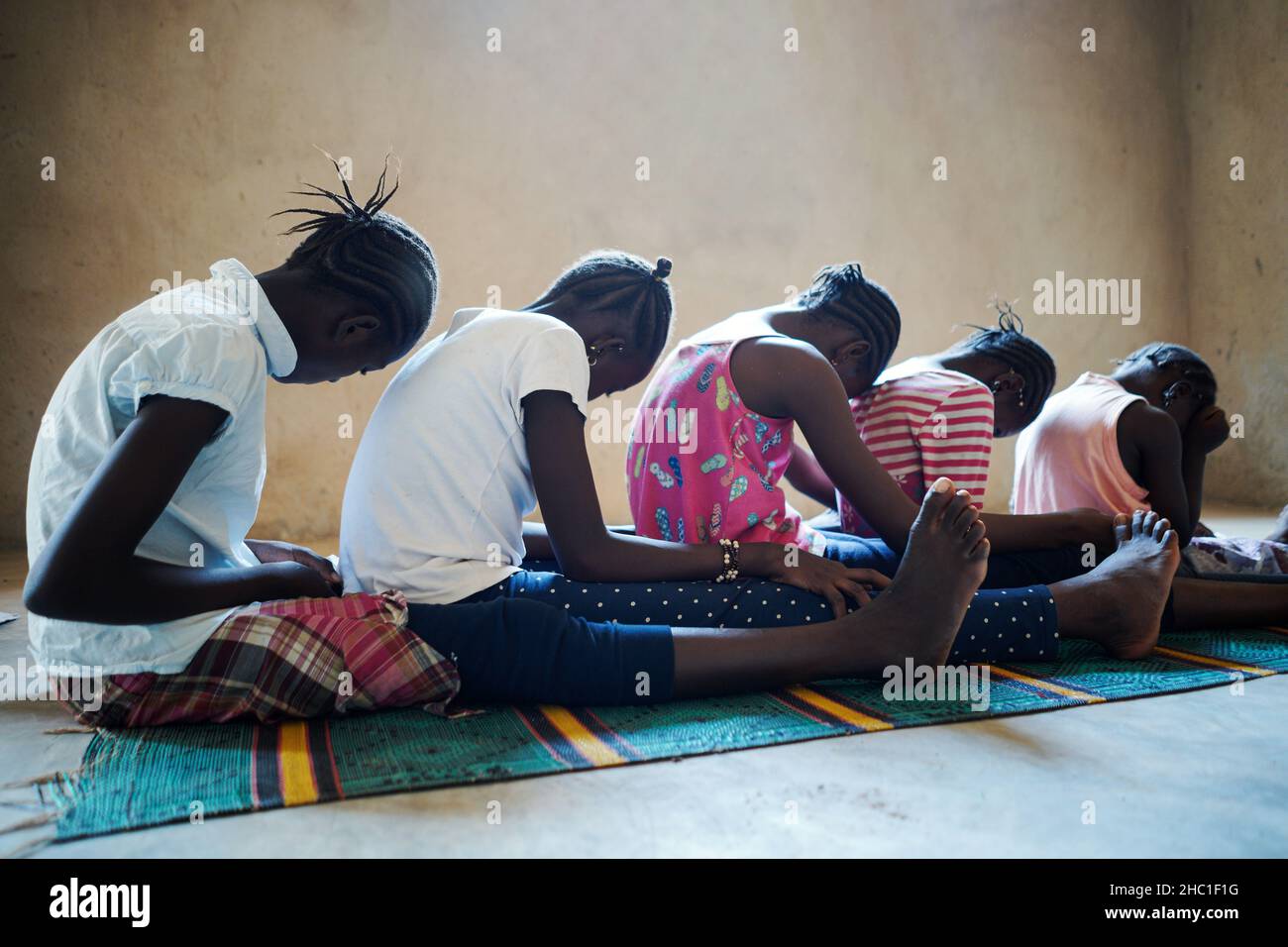Vista laterale di un gruppo di spaventate ragazze nere africane del villaggio che siedono sul pavimento in attesa del loro turno durante un rituale collettivo di circoncisione Foto Stock