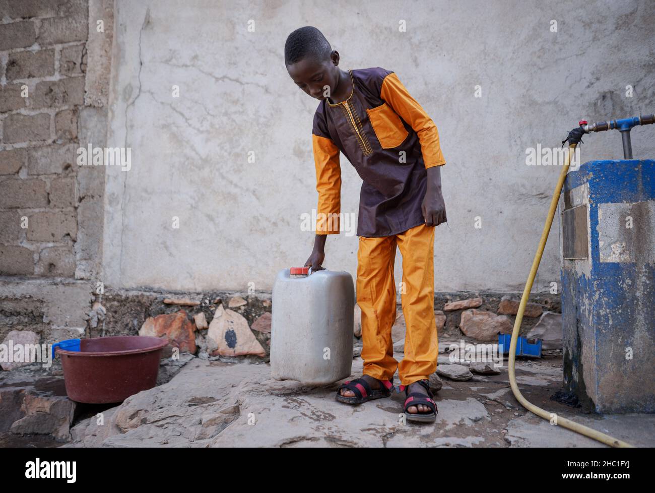 Giovane ragazzo nero vestito ordinatamente che attingeva l'acqua della sua famiglia a un rubinetto pubblico in Africa occidentale; mancanza di infrastrutture idriche in sviluppo Foto Stock
