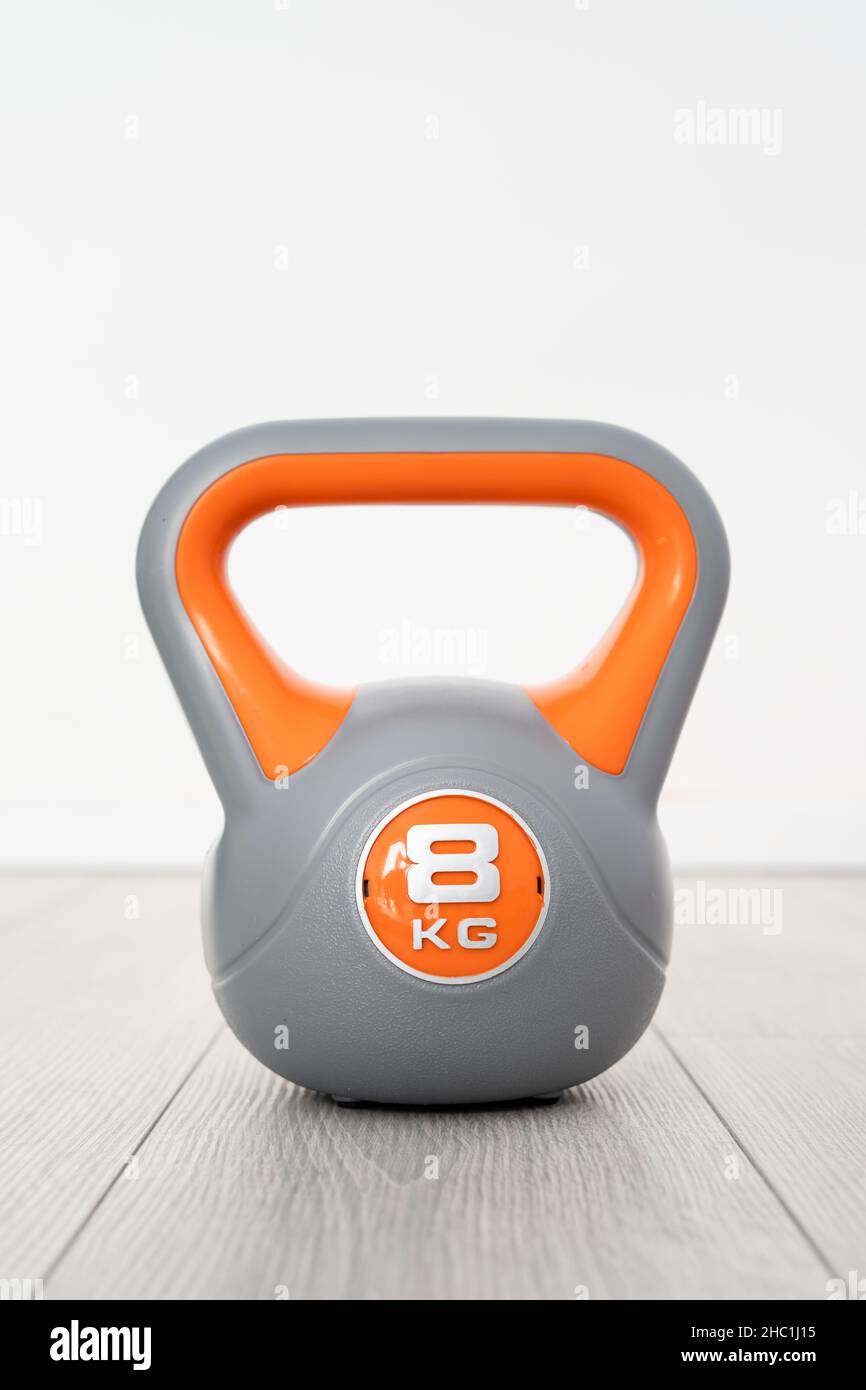Un kettlebell in plastica da 8 kg di materiale didattico grigio e arancione sul pavimento Foto Stock Un kettlebell in plastica da 8 kg di materiale didattico grigio e arancione sul pavimento Foto Stock