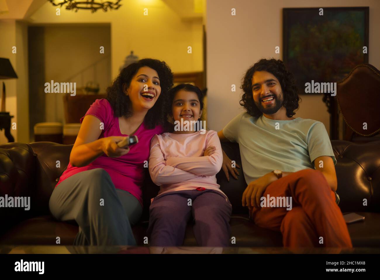 Donna che guarda la televisione con la figlia e il marito e che tiene il telecomando Foto Stock