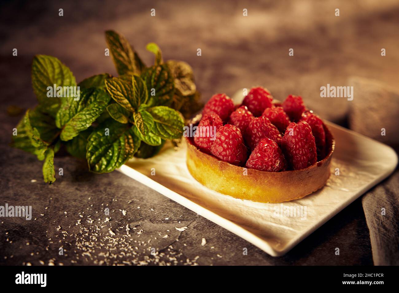 Cestino per torte con lamponi su un piatto di ceramica bianca con foglie di menta su sfondo scuro Foto Stock