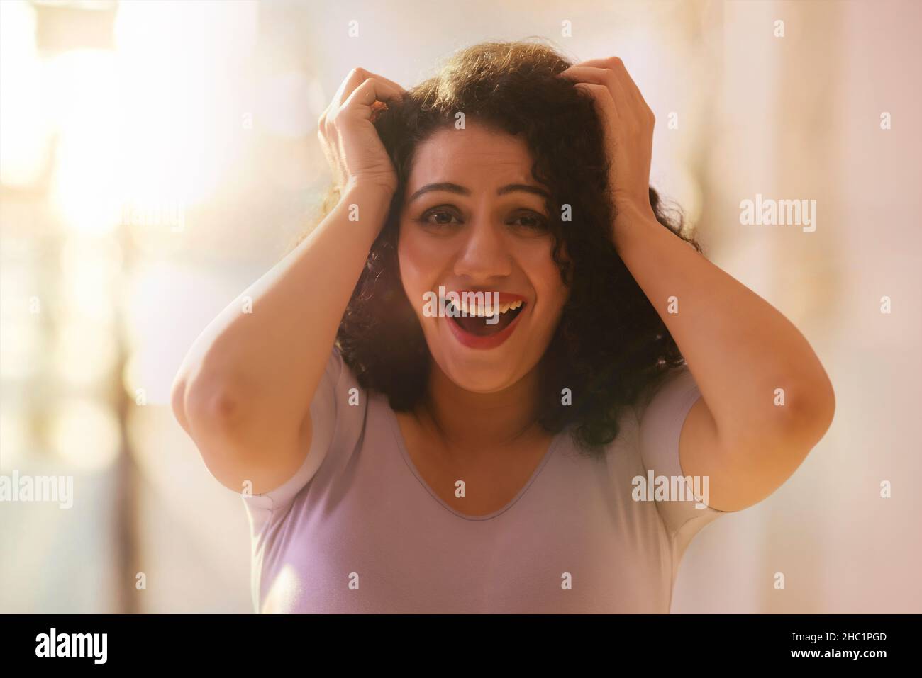 Giovane donna adulta che ride con entrambe le mani sulla testa Foto Stock
