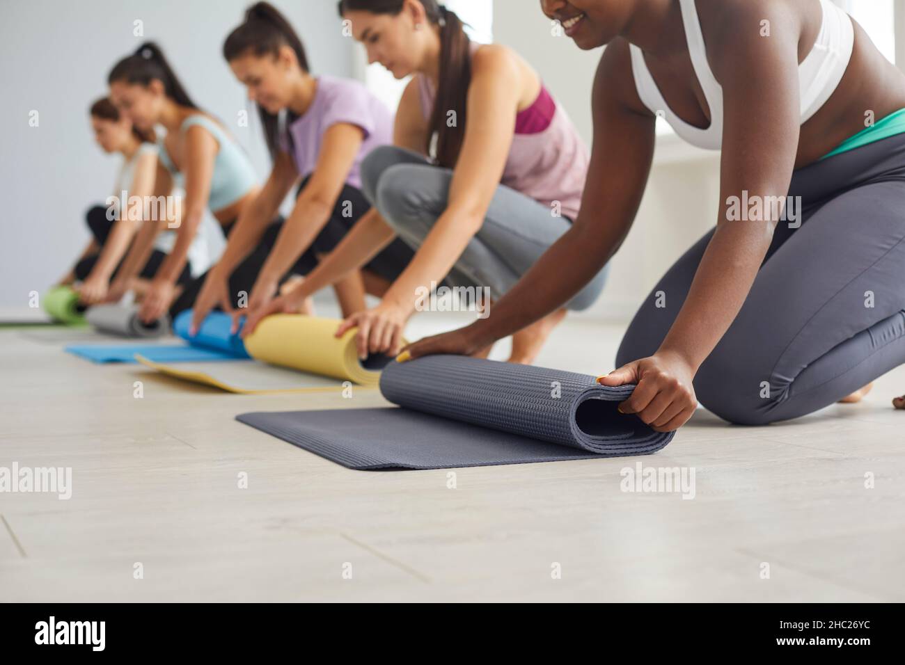 Gruppo di ragazze felici che arrotolano i tappetini di gomma dopo la pratica di yoga o l'allenamento di idoneità alla palestra Foto Stock