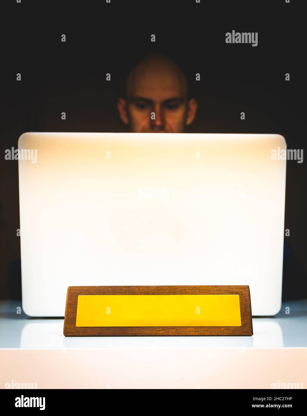 Persona seduta dietro il computer portatile su sfondo nero con la piastra in legno per la posizione dell'ufficio nel rinuncio. Concetto di lavoro da casa. Foto Stock