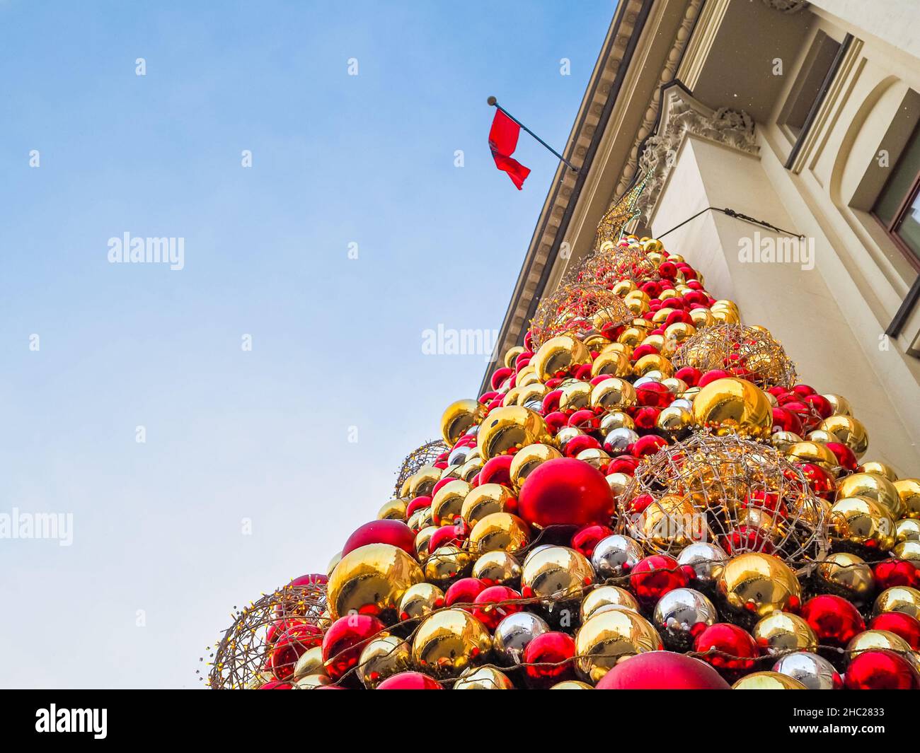 Vista dal basso dell'installazione di palle lucide multicolore di Capodanno sulla facciata dell'edificio. Messa a fuoco selettiva. Decorazioni natalizie sull'edificio della città. Foto Stock