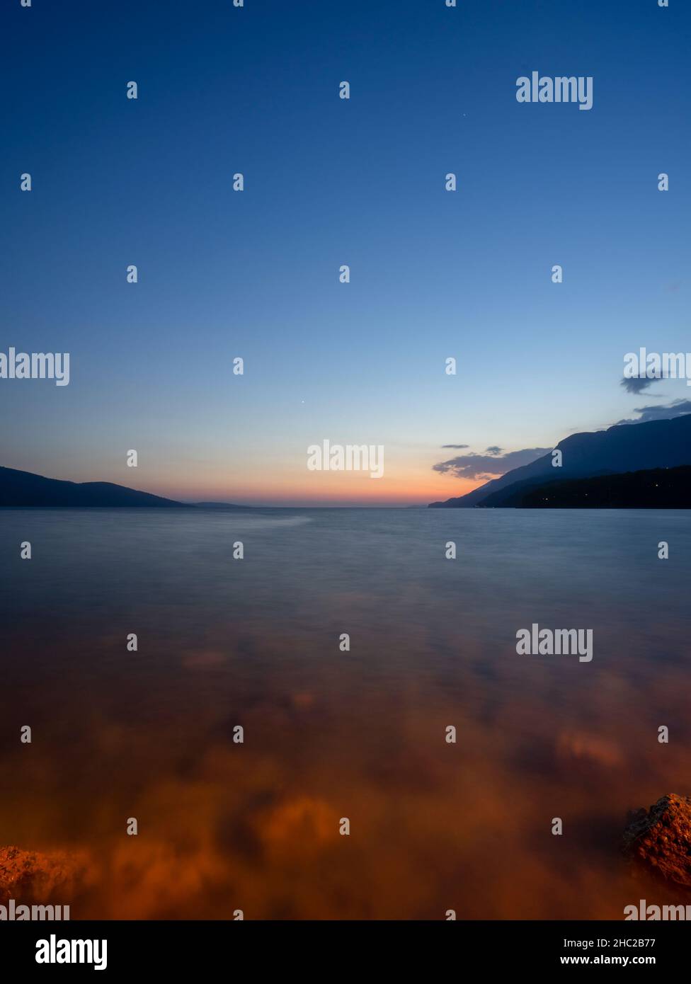 Lunga esposizione del mare ad un'ora blu su una spiaggia rocciosa. Vista al tramonto del Golfo di Gokova (Akyaka), Mugla, Turchia. Foto Stock
