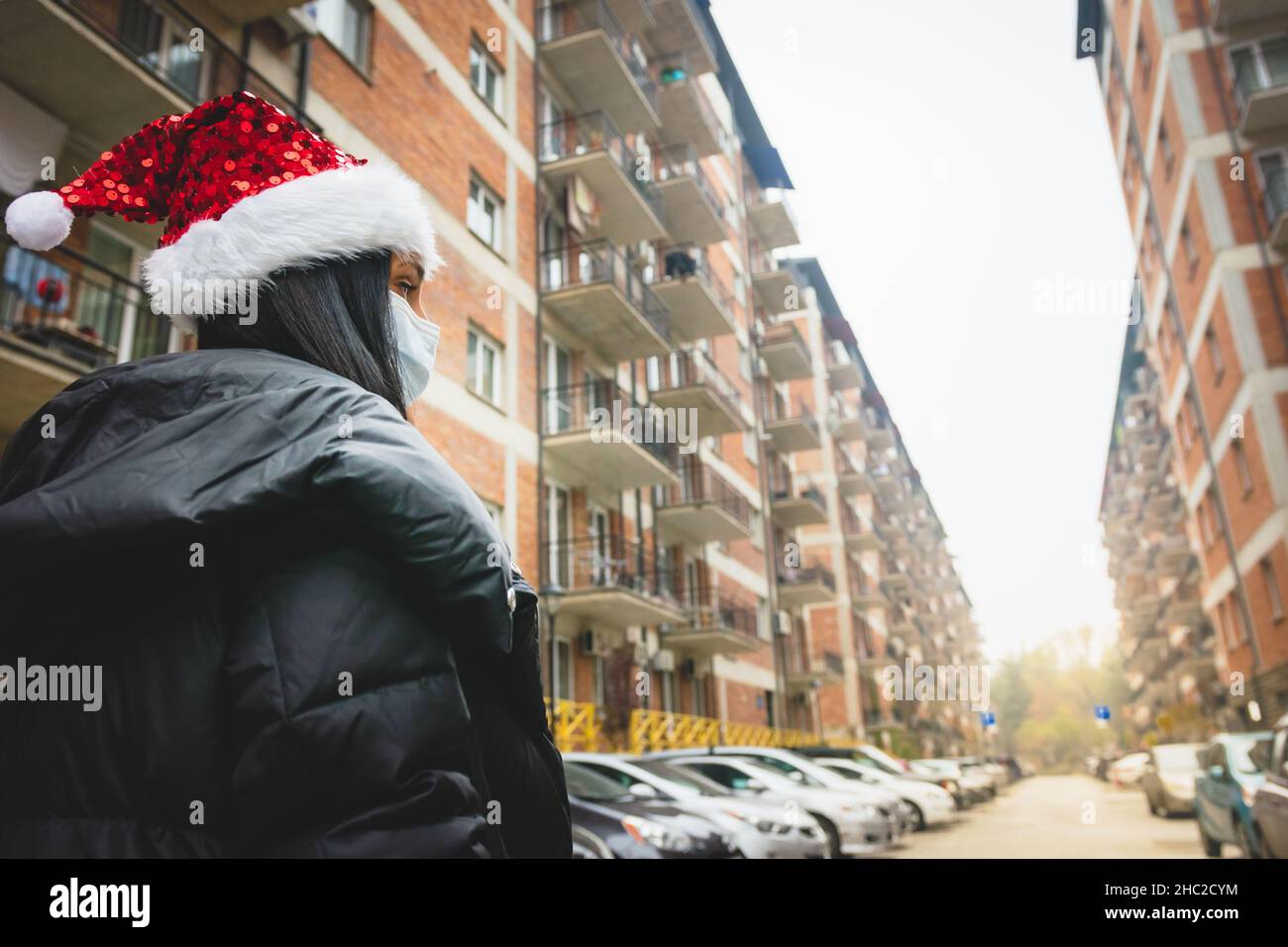 Donna in vacanza stagione guarda a destra con vista sulla strada e case sullo sfondo. Natale a casa in quarantena e coprifuoco a Natale. Foto Stock