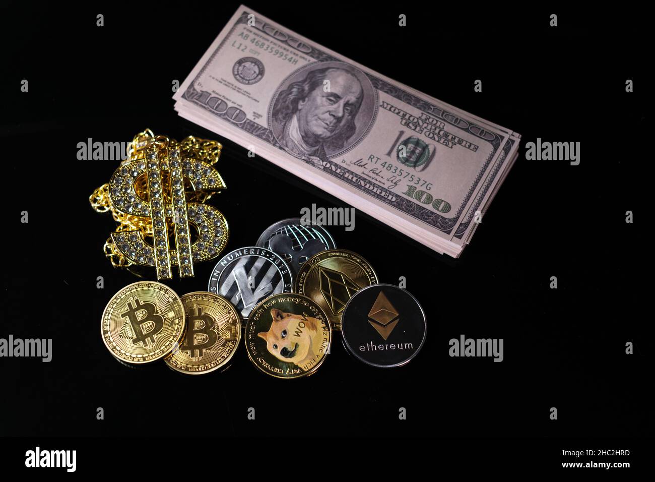 alcune monete di cripto si trovano vicino ad una pila di 100-dollaro fatture, un orologio di allarme bianco ed un pendente della catena del dollaro del diamante-chiodati Foto Stock