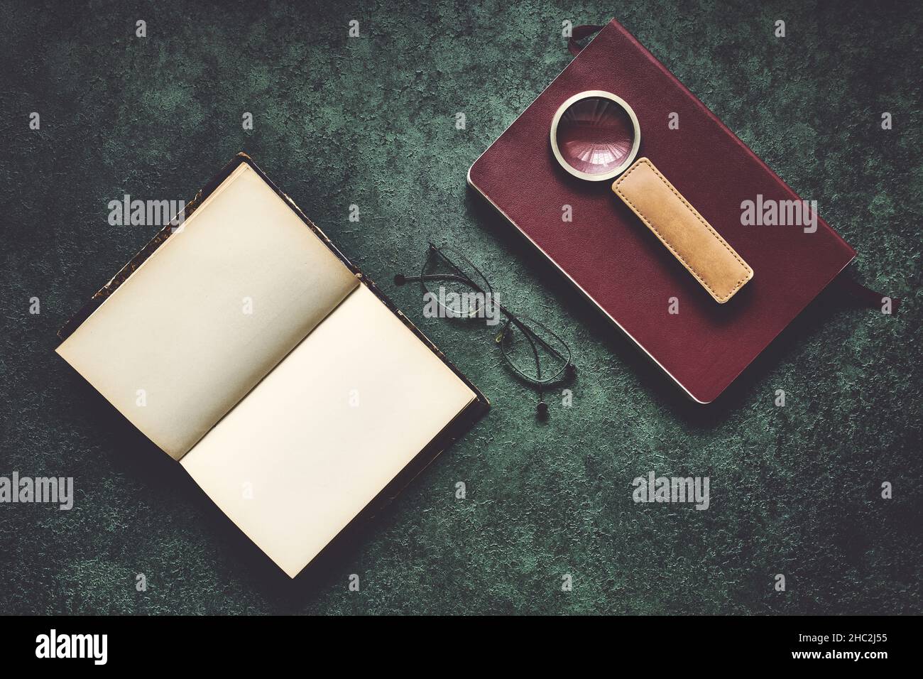 Vecchi libri, occhiali e una lente d'ingrandimento con manico in pelle, scuro e moody, vista dall'alto Foto Stock