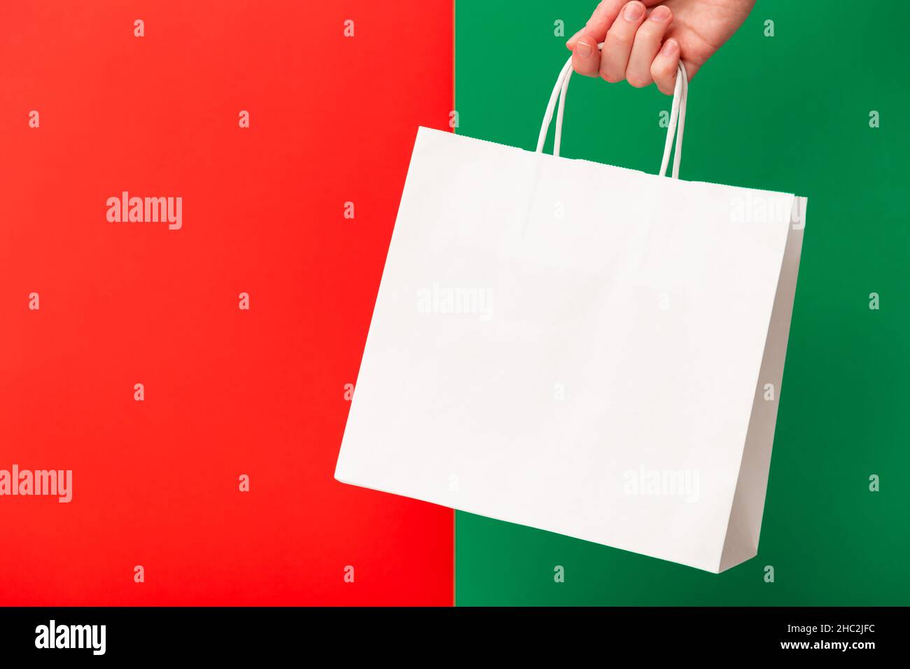 Donna mano che tiene bianco shopping bag isolato su sfondo rosso e verde. Offerta Black friday, vendita natalizia, sconto, shopping ed ecologia c Foto Stock