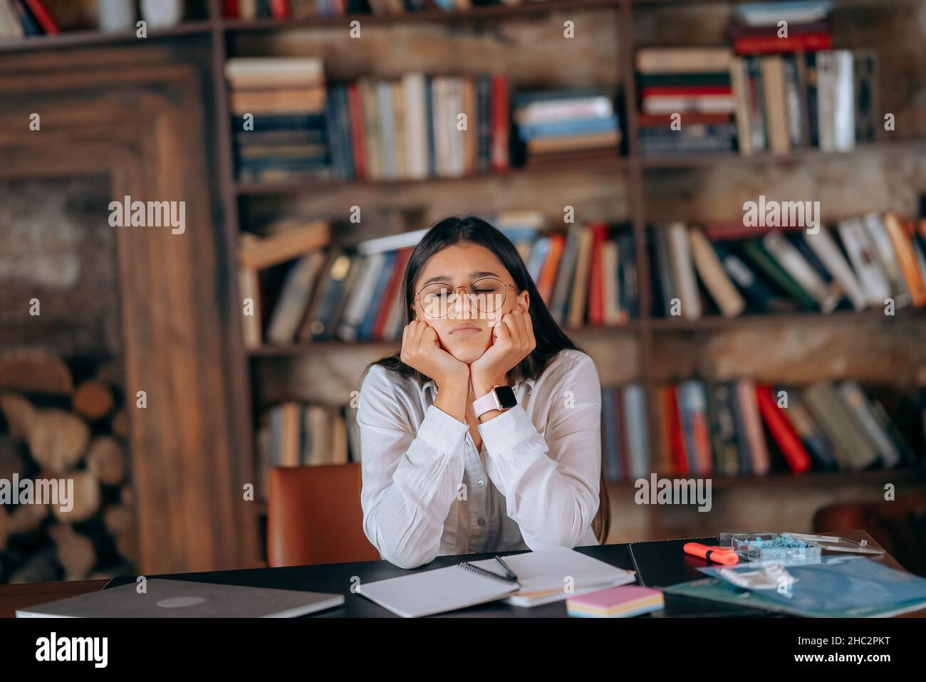 Giovane donna in ufficio che pensa al problema sullo sfondo delle librerie Foto Stock
