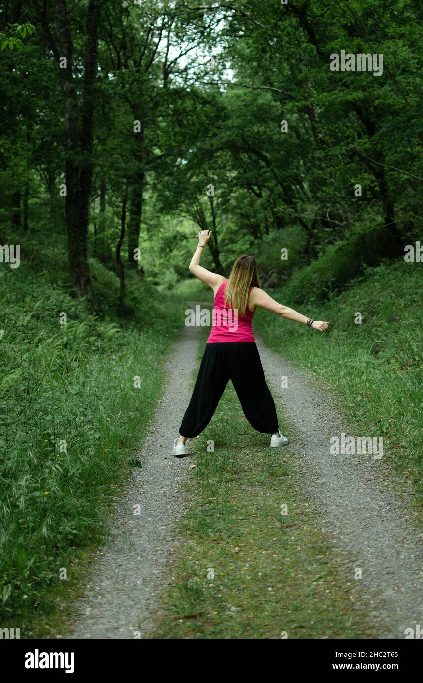 la bionda cammina tra i boschi, indossa una maglietta turchese, la ragazza sta ballando Foto Stock