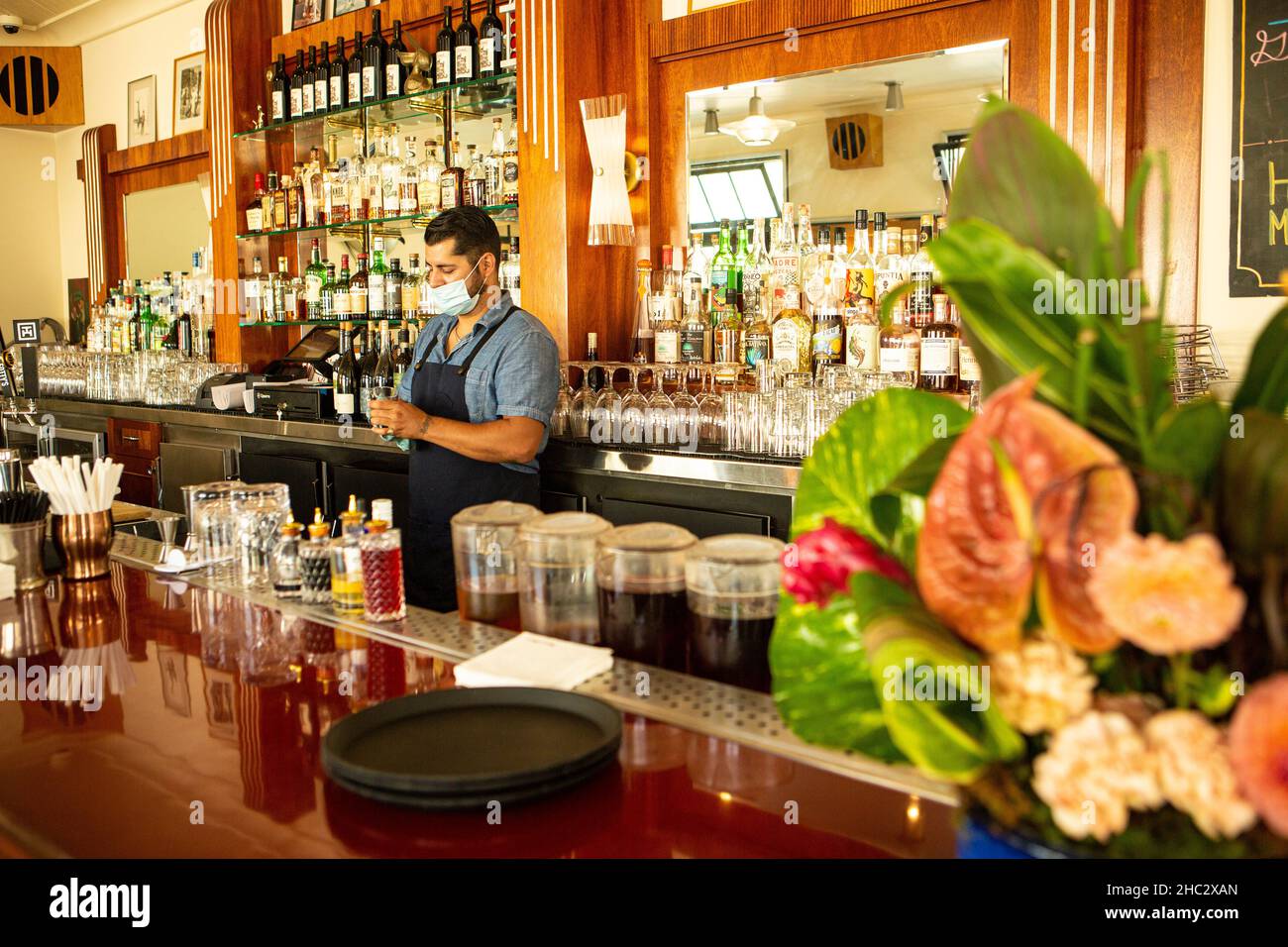 Il barman che indossa una maschera per la protezione COVID pulisce gli occhiali Foto Stock