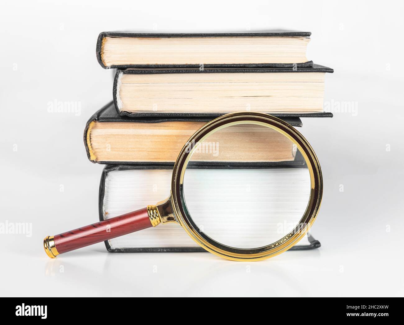 Lente d'ingrandimento e pila di libri. Concetto di conoscenza, ricerca accademica e studio. Lente d'ingrandimento e libri di testo. Foto Stock