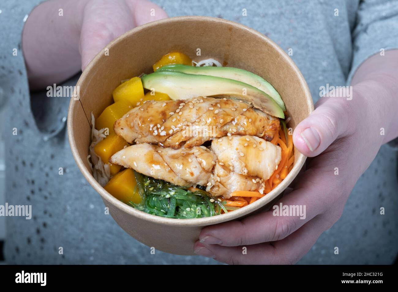 Helsinki / Finlandia - 12 DICEMBRE 2021: Una donna caucasica che tiene una ciotola di cartone di insalata asiatica fresca. Foto Stock