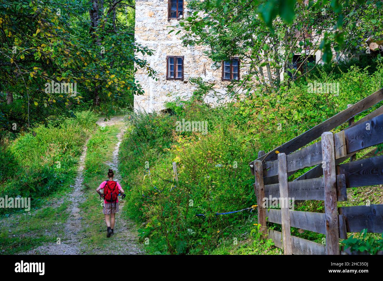 La donna escursionistica passa accanto a una vecchia casa di pietra durante un'escursione vicino a Kranjska Gora, alpi slovene Foto Stock