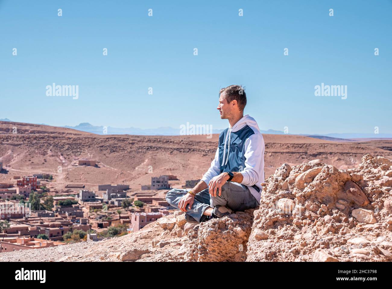 Giovane uomo che guarda la vista mentre si siede su roccia contro terra e cielo deserti Foto Stock