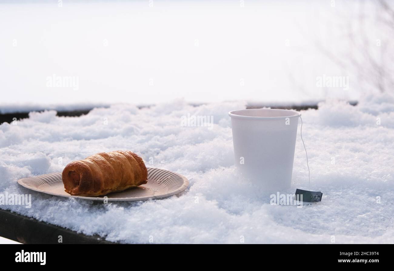 Tazza di carta bianca con tè caldo su tavola innevata. Foto Stock
