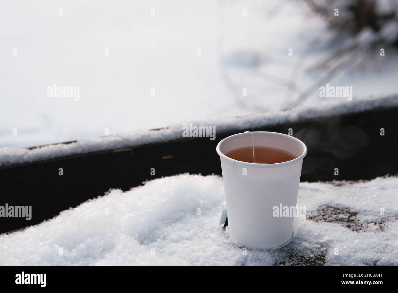 Tazza di carta bianca con tè caldo su tavola innevata. Foto Stock