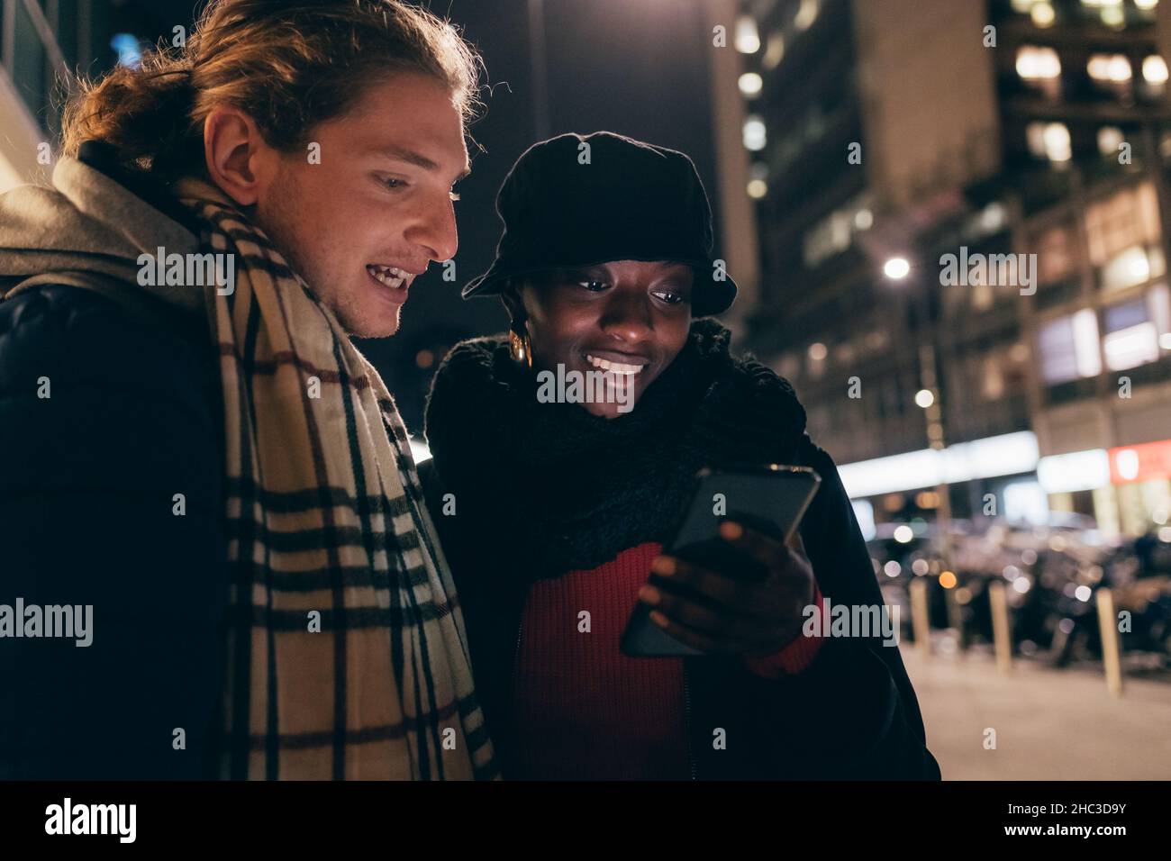 Italia, coppia sorridente che guarda lo smartphone in città di notte Foto Stock