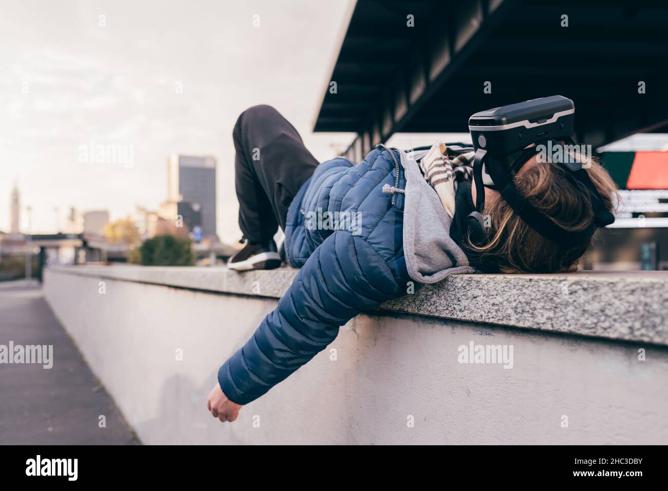 Italia, uomo con occhiali di protezione per la realtà virtuale sdraiato sul muro della città Foto Stock