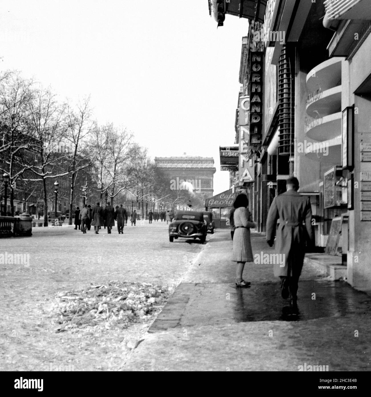 Paris Avenue des Champs-Elysees a Metro George V guardando verso l'Arco di Trionfo in inverno, 1945. Una delle due fotografie che raffigurano le persone che camminano e le imprese intorno alla metropolitana con la neve sul terreno. Non ci sono quasi veicoli in vista e le foto sono state scattate quando gli Champs-Elysees avevano ancora dei mediani alberati che restringevano il viale in una scala pedonale migliore. Molte delle persone fuori sono in uniforme militare. Le aziende raffigurate lungo il lato nord-est del viale includono il Café George V, il Normandie, Milady, Lord Byron e il cinema. Gli alberi sono pieni di neve. Foto Stock