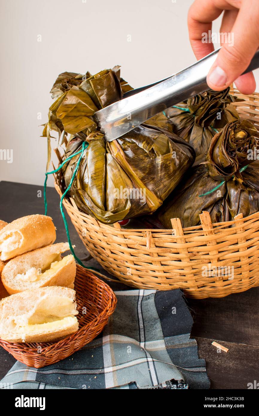 Prendere a mano un tradizionale cibo colombiano noto come 'tamal' avvolto con foglie da un cestino su un tavolo nero Foto Stock
