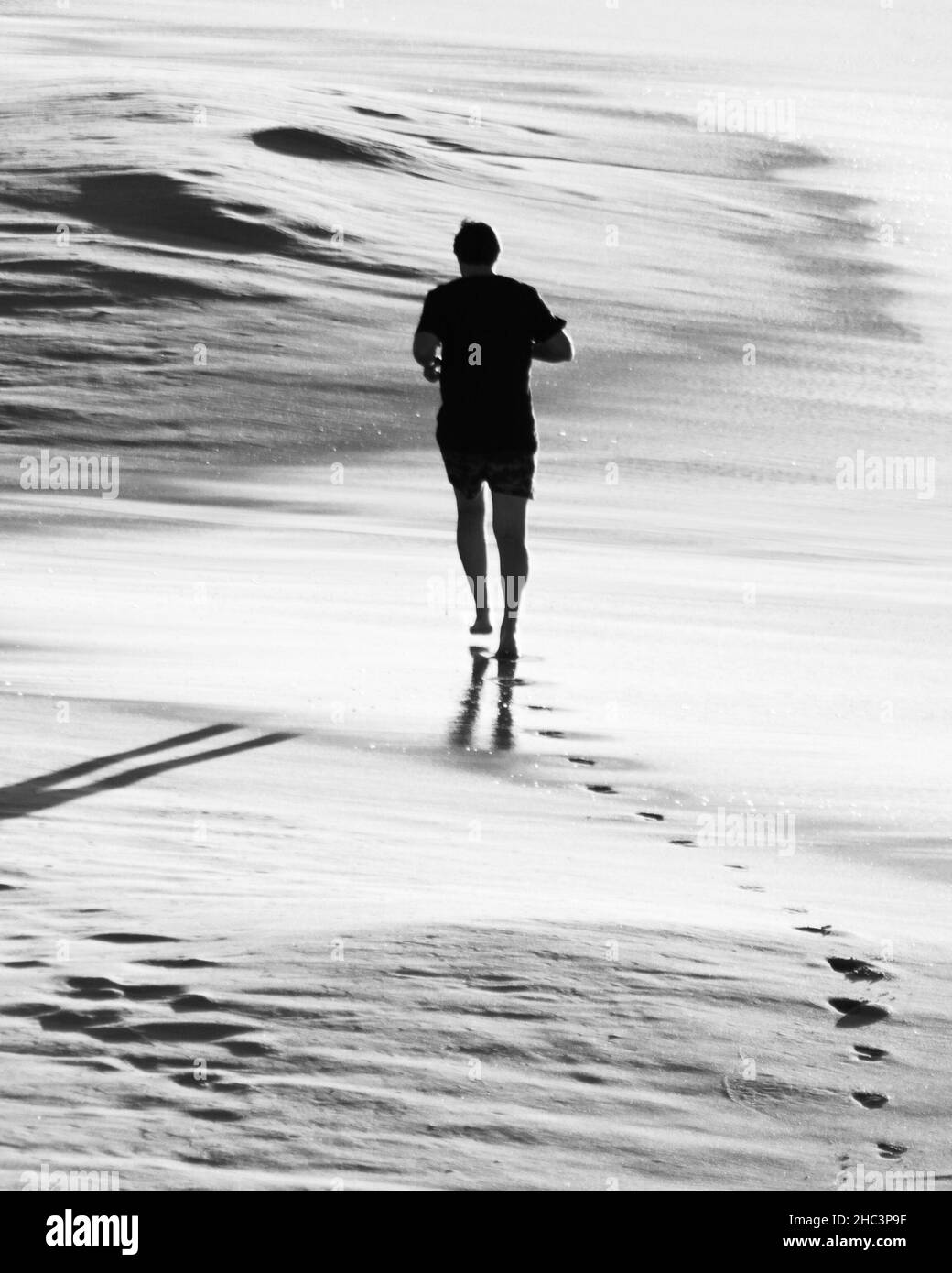 Scatto monocromatico di un giovane uomo che corre su una spiaggia sabbiosa, vista posteriore Foto Stock