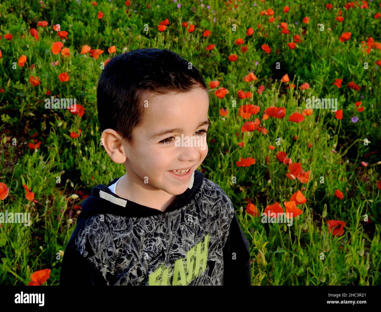 ragazzo felice con un grande sorriso giocando in un campo di papavero in una giornata di primavera soleggiata Foto Stock
