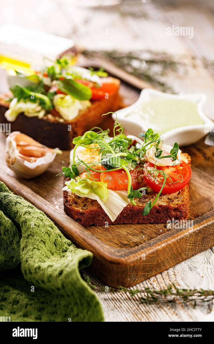 Toast da primo piano con pesce salato, formaggio, uova, anelli di cipolla e insalata. Stuzzichini o sandwich appetitosi con salmone affumicato. Colazione deliziosa Foto Stock