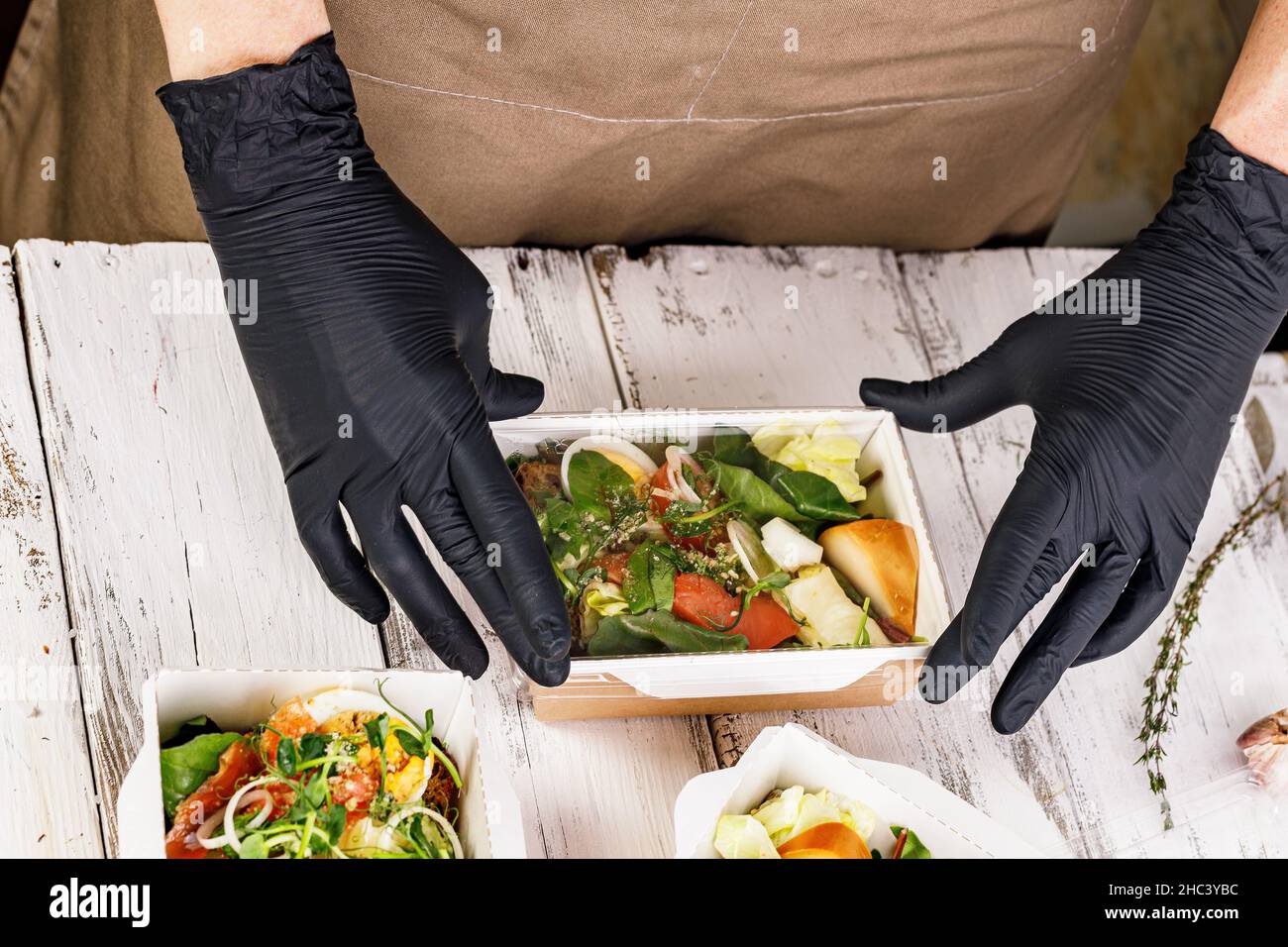 Le mani in guanti neri stanno imballando un pranzo di affari in una scatola di cartone. Concetto di servizio di consegna di cibo. Cibo delizioso e sano sul posto di lavoro. Tak Foto Stock
