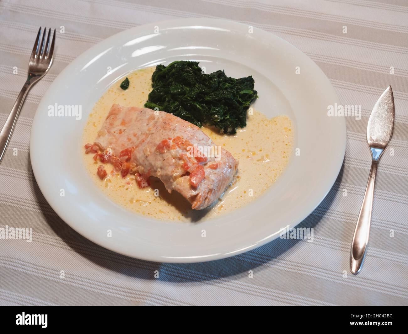 Salmone in salsa alla panna con spinaci al burro su un piatto bianco con coltello di pesce d'argento e forchetta Foto Stock