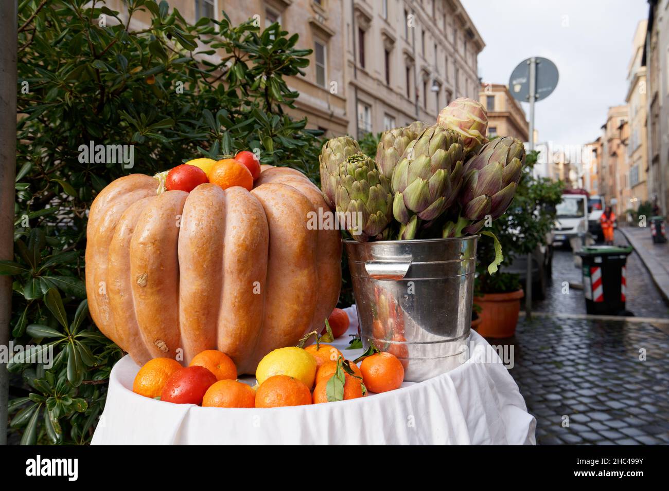 Fuoco selettivo sparato di una zucca, carciofi e altri prodotti con edifici sul retro Foto Stock