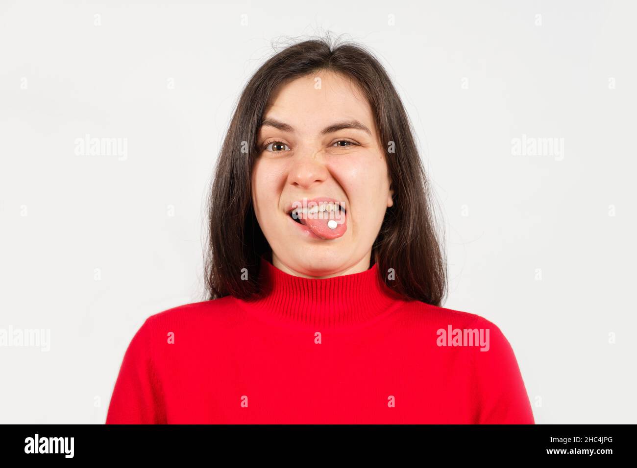 Una donna in un maglione rosso con una pillola bianca sulla sua lingua con la bocca aperta, con una grimace disgruntled Foto Stock