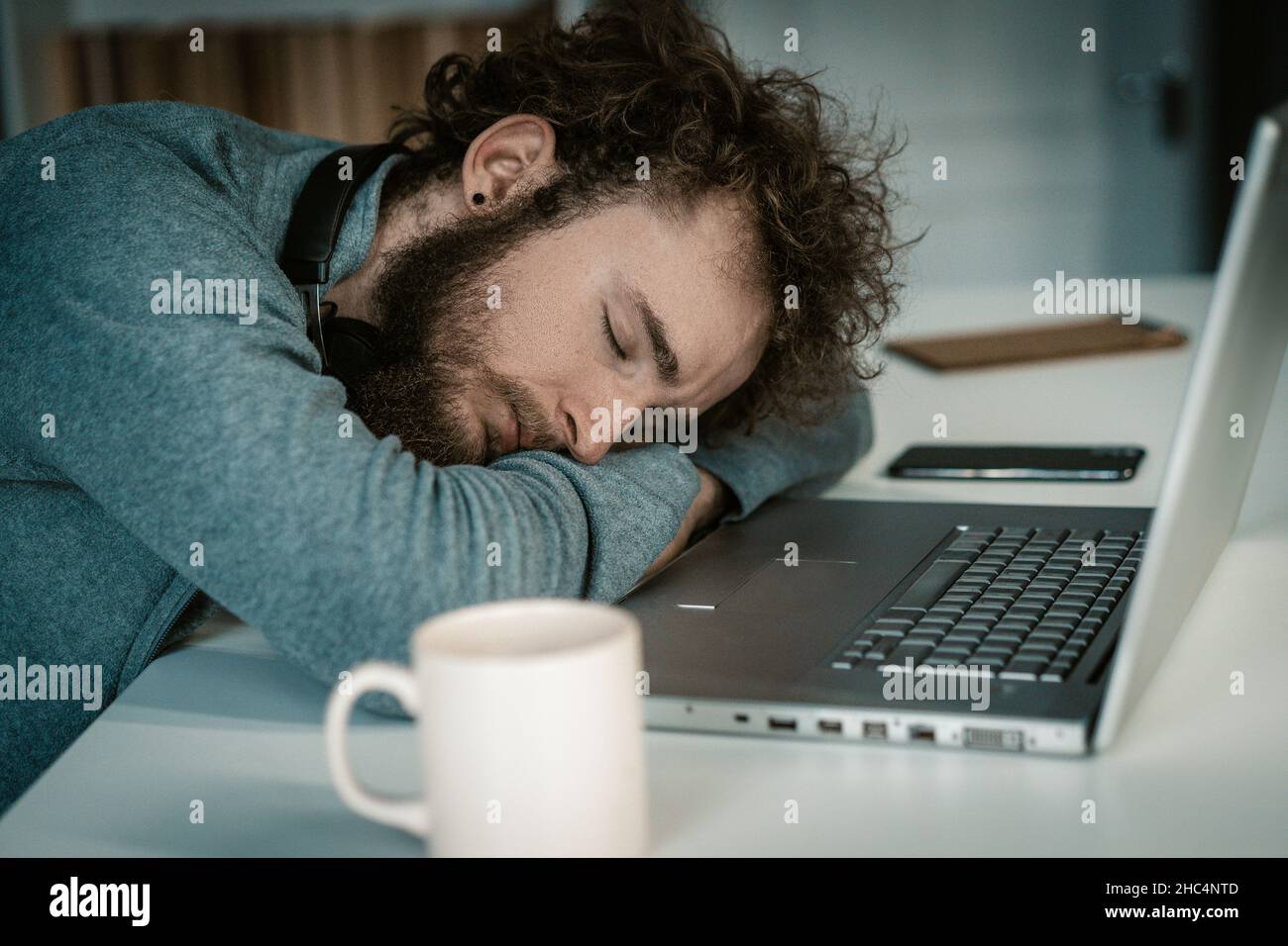 L'uomo con le mani ripiegate dorme sulla scrivania con il laptop. Dormi seduto, Freelance di notte, tazza di caffè sul tavolo. Primo piano. Foto di alta qualità Foto Stock