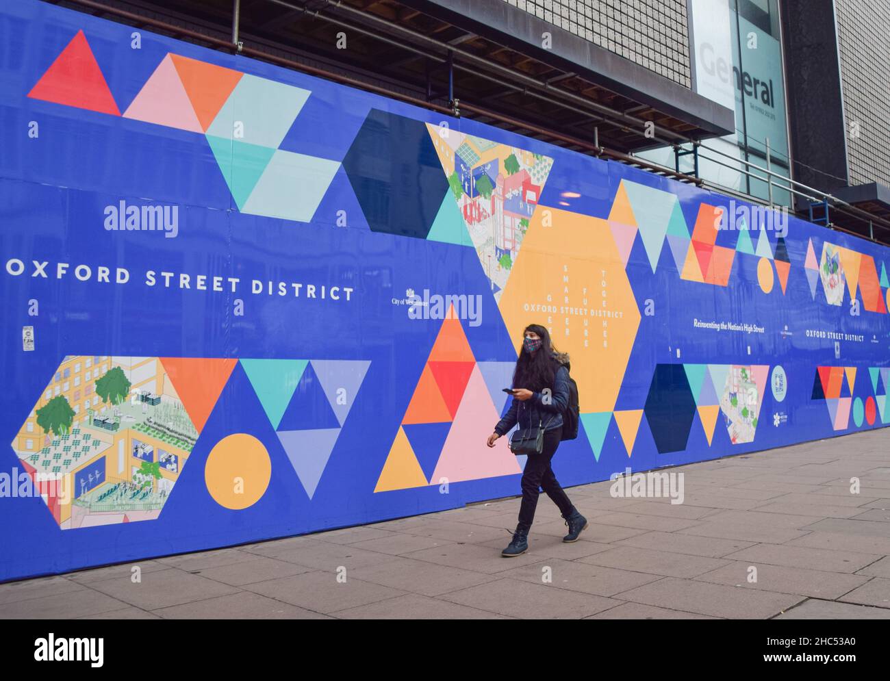 Una donna che indossa una maschera protettiva per il viso passa accanto all'ex sito di ristrutturazione del negozio di punta Debenham su Oxford Street. Londra, Regno Unito 24 dicembre 2021. Foto Stock