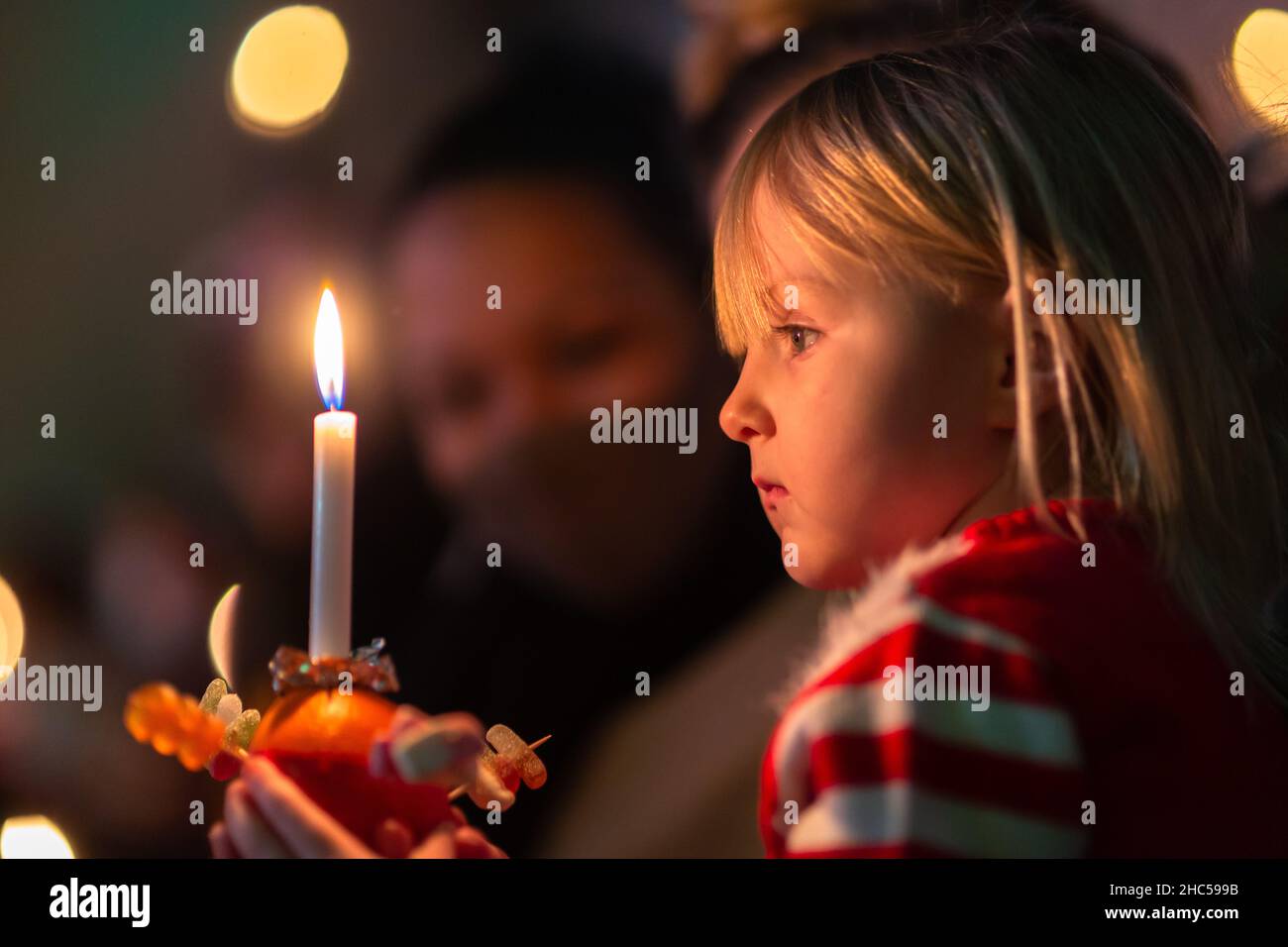 Old Hill, West Midlands, Regno Unito. 24th Dic 2021. Harlow Leigh-Fowkes, 4 anni, tiene il suo arancio di Christingle durante il servizio di Christingle della vigilia di Natale presso la Holy Trinity Church, Old Hill nelle West Midlands. Le Christingles sono arance avvolte in nastro rosso, decorate con frutta secca o dolci, con una candela sulla parte superiore. Credit: Peter Lopeman/Alamy Live News Foto Stock