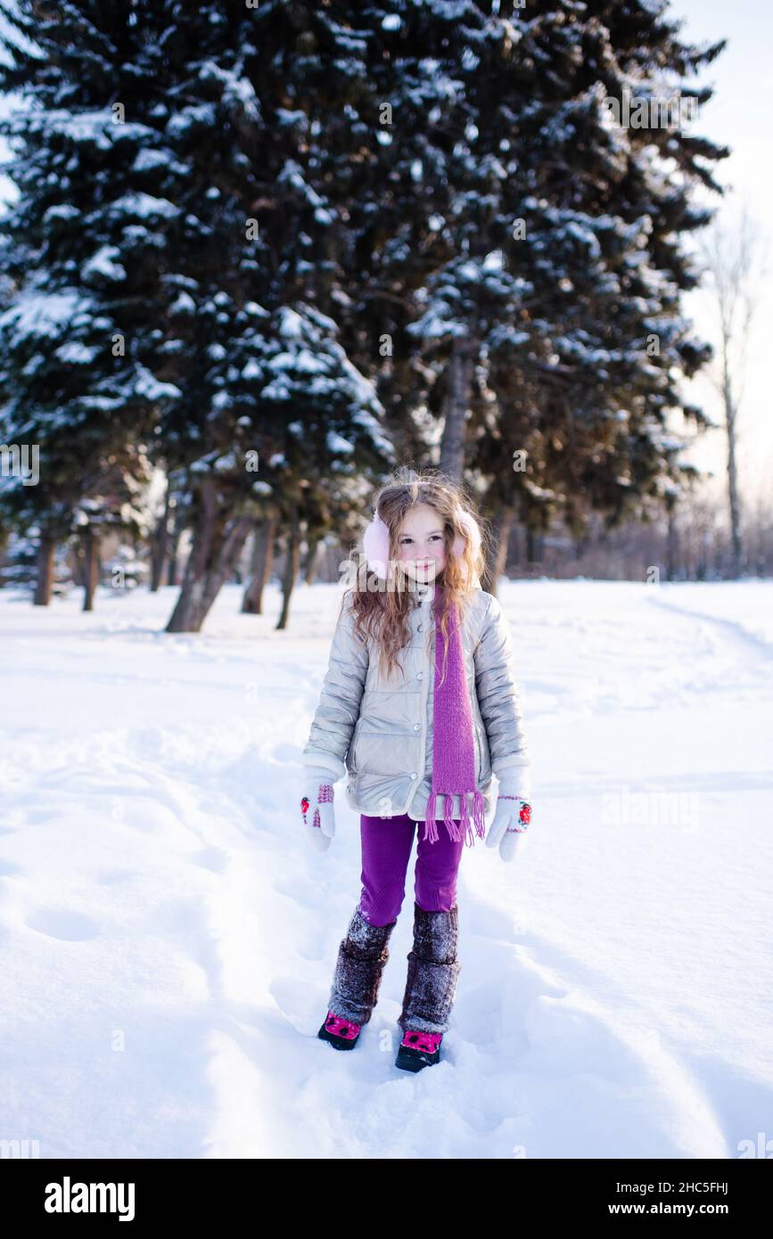 Carino ragazza divertente bambino 5-6 anni a piedi nel parco nevoso sopra la natura sfondo all'aperto. I bambini indossano giacca invernale, sciarpa e cuffie all'esterno. CH Foto Stock