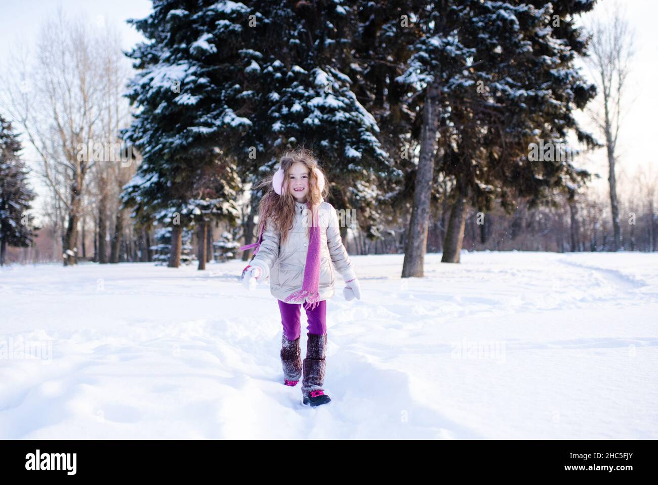Carino ragazza divertente bambino 5-6 anni a piedi nel parco nevoso sopra la natura sfondo all'aperto. I bambini indossano giacca invernale, sciarpa e cuffie all'esterno. CH Foto Stock