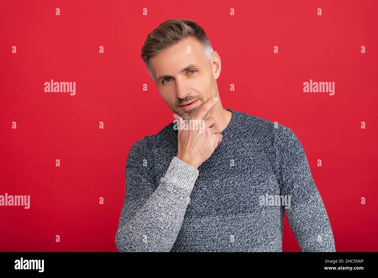 ragazzo grizzled in maglione su sfondo rosso. ritratto di uomo con barba. modello di moda maschile. Foto Stock