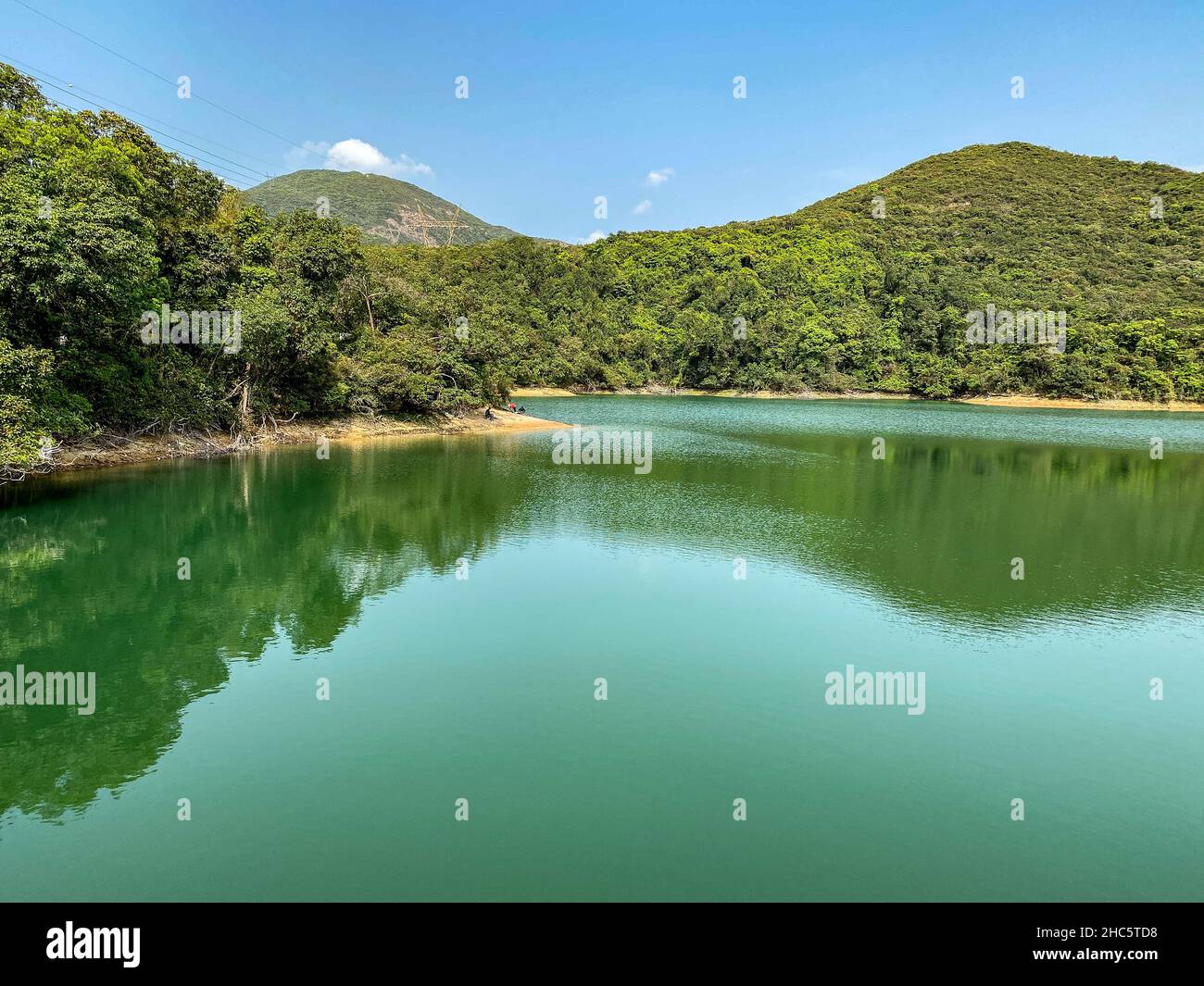 Bellissimo scatto di un lago limpido circondato da colline coperte di verde Foto Stock