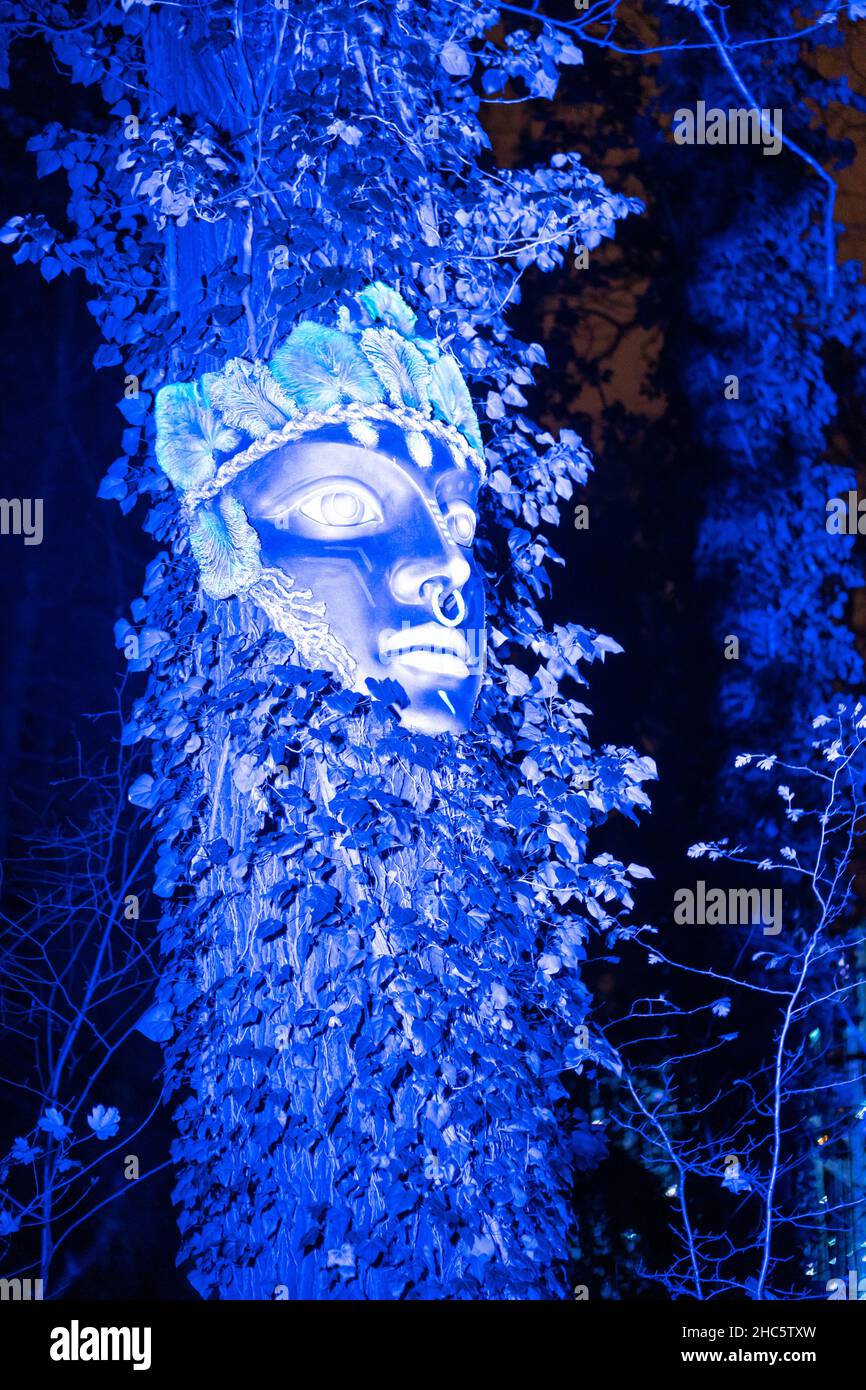 Un primo piano verticale di una maschera con luci blu su un albero nella notte al Parco Lumina Foto Stock