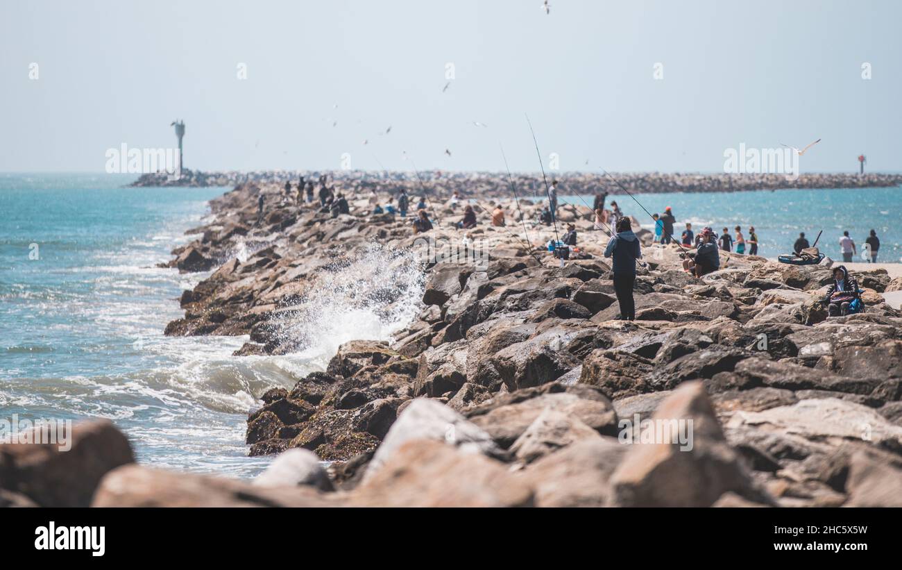 Scatto panoramico di numerose persone che pescano sulla riva dell'oceano Foto Stock