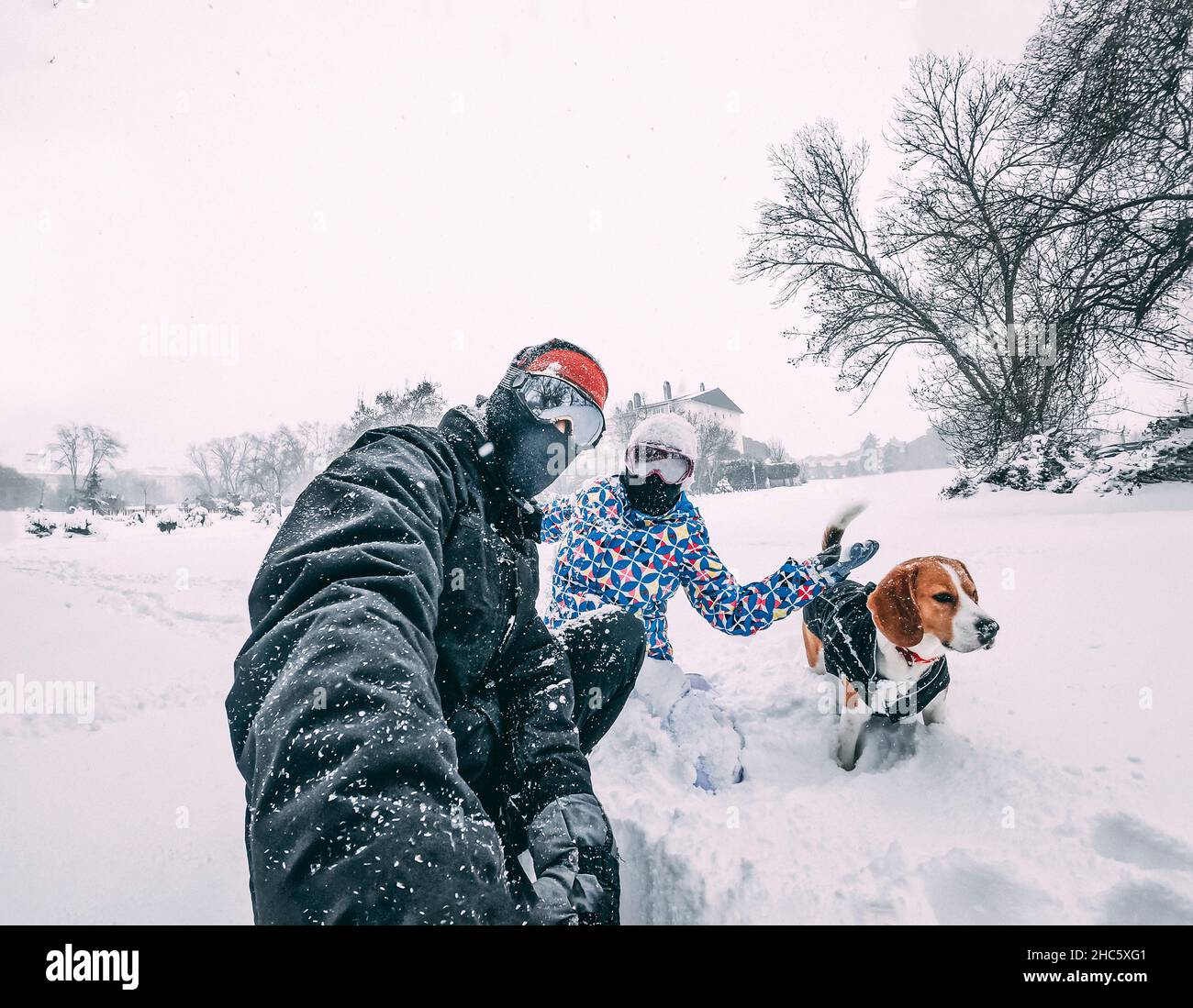 Coppia felice con il loro cane beagle, prendendo un selfie durante una tempesta di neve, dotato di abbigliamento invernale, closeup, concetto di vacanza Foto Stock