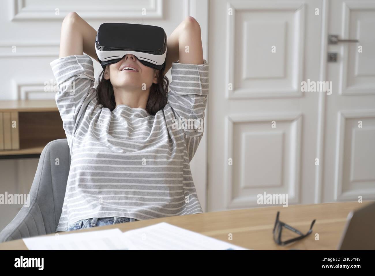 Giovane donna felice in occhiali per la realtà virtuale sul posto di lavoro guardando i film Foto Stock